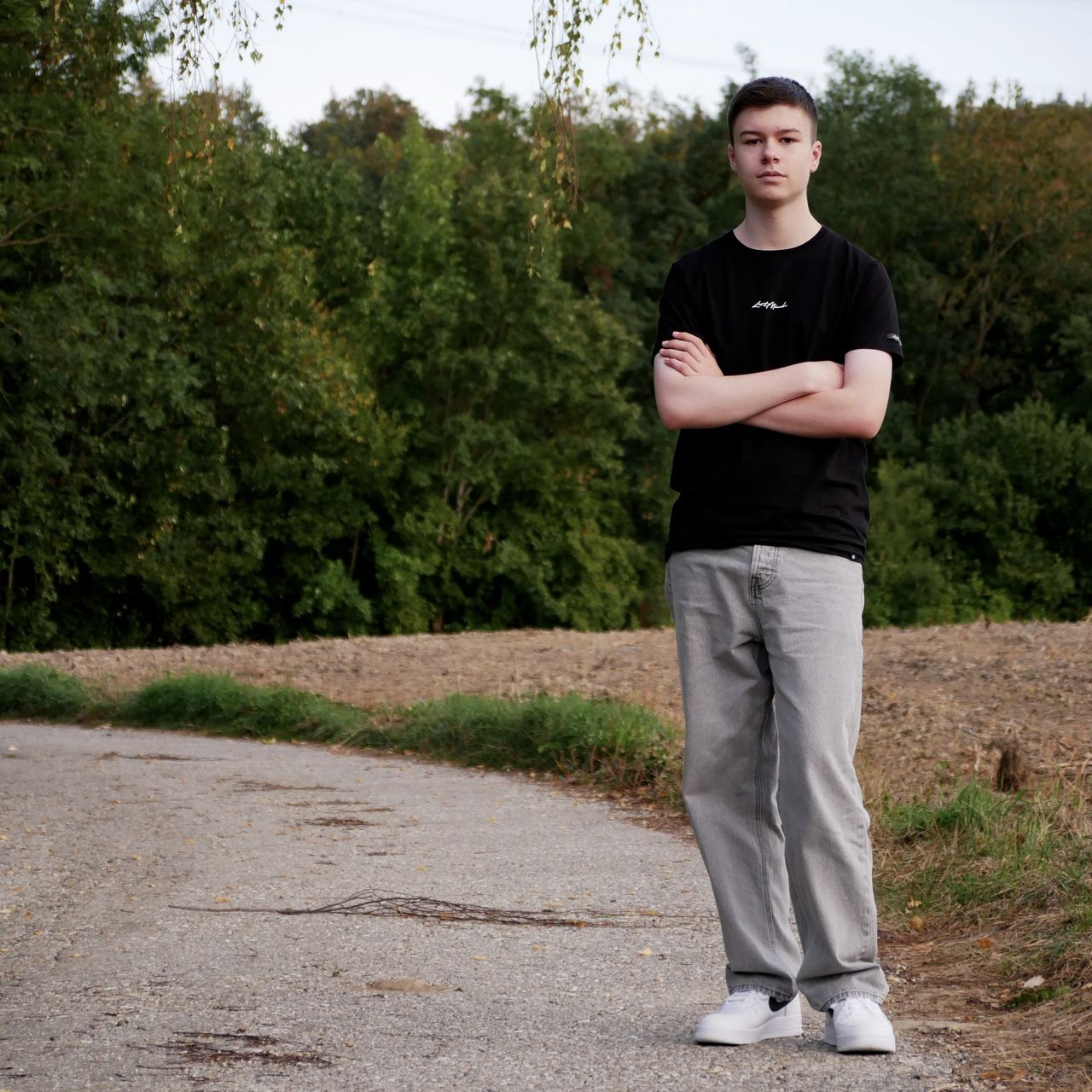 Tobi mit verschränkten Armen auf einem Feldweg, Bäume hinter ihm