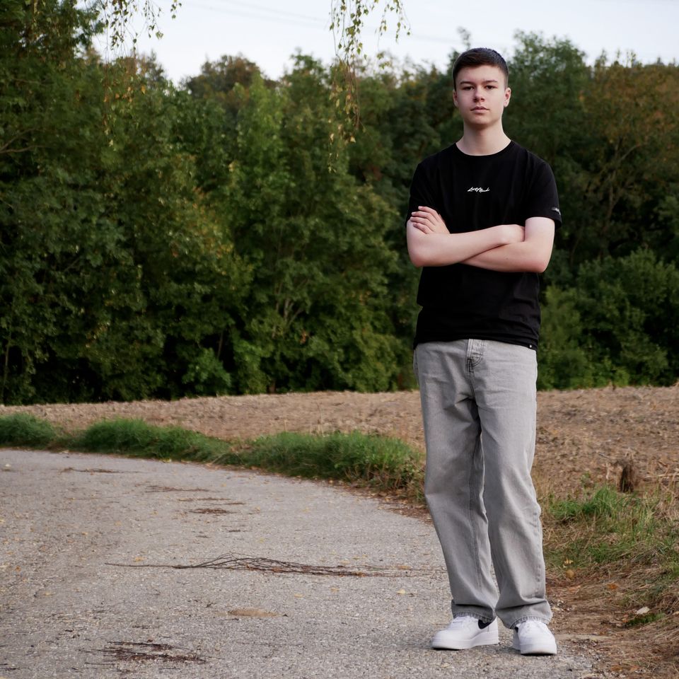 Tobi with his arms crossed on a country lane, trees behind him