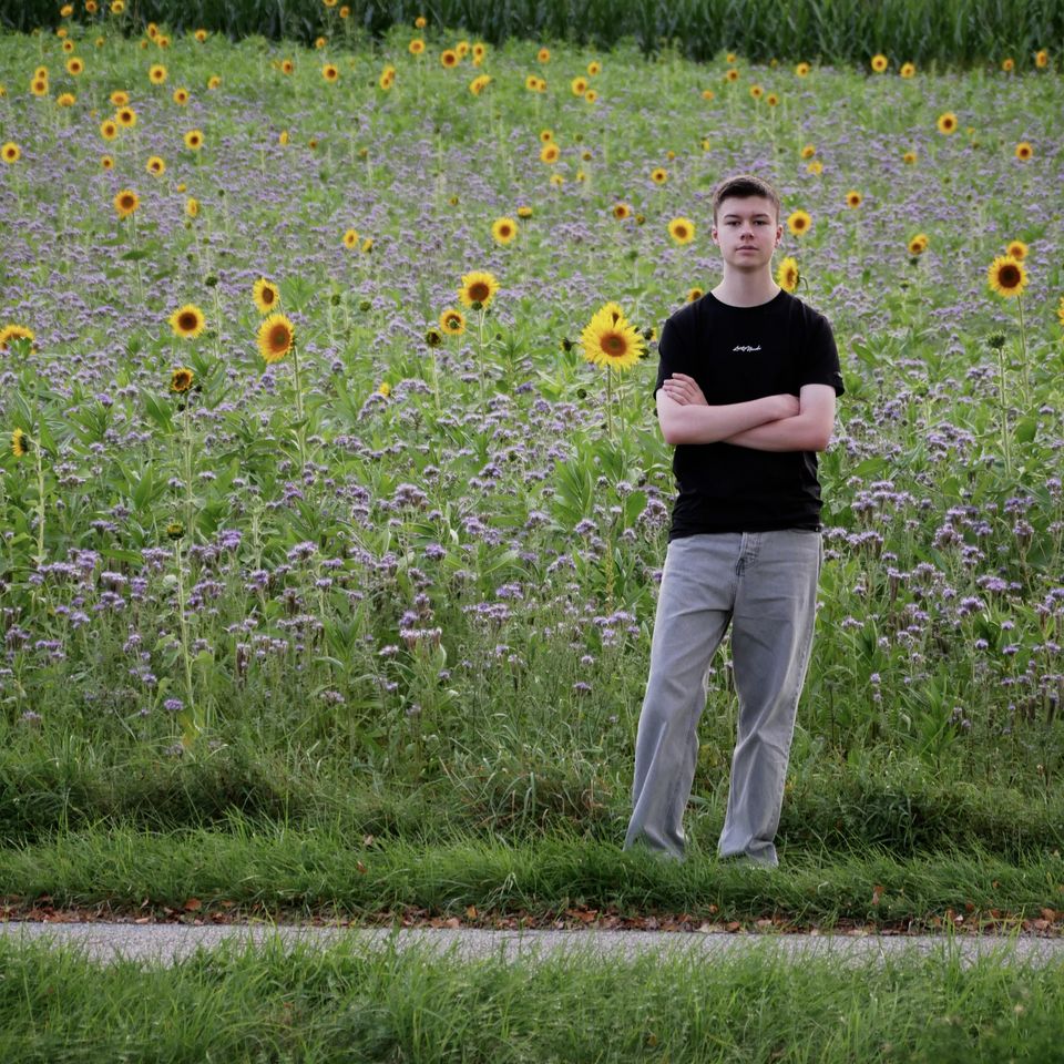 Tobi with his arms crossed in front of a field of sunflowers and purple flowers