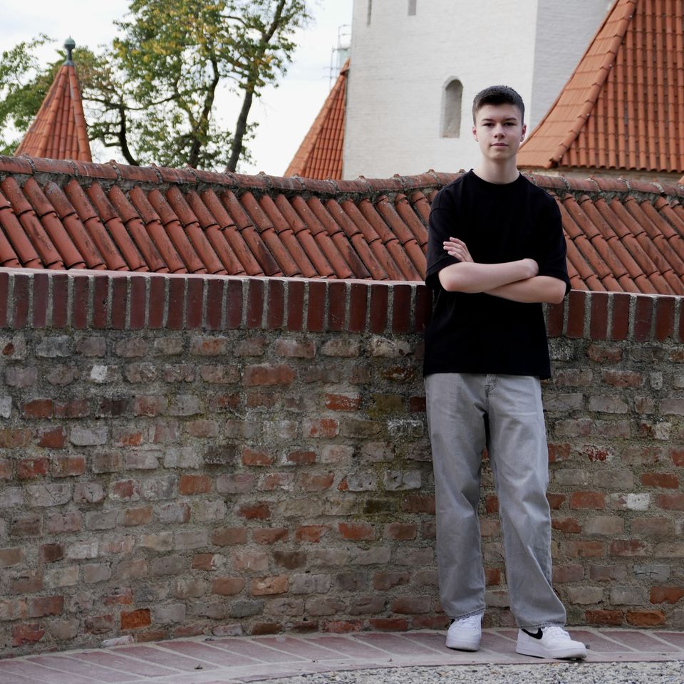 Tobi with his arms crossed in front of a brick wall and red tiled roofs